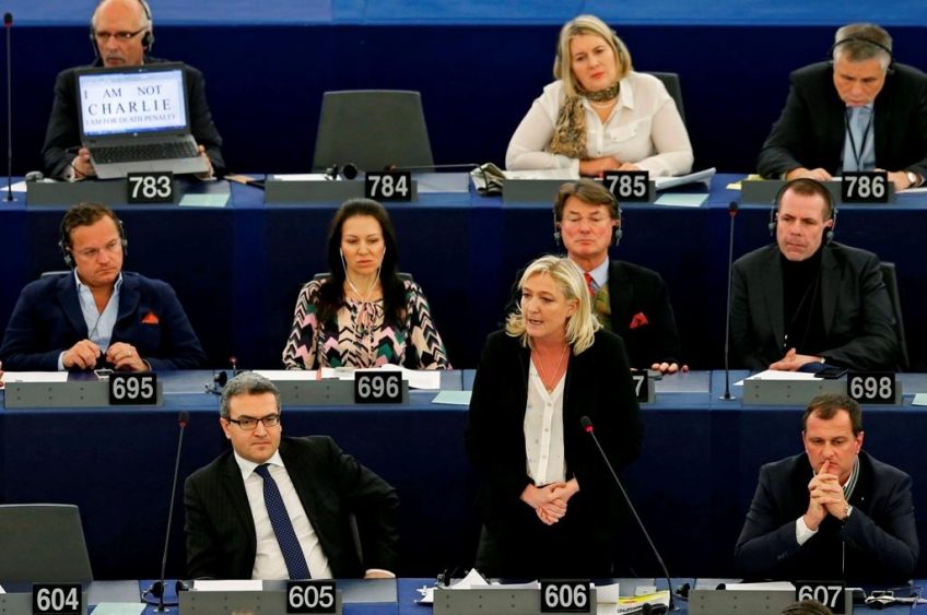 France's National Front political party head Marine Le Pen (Standing) delivers a speech as fellow Polish Member of the European Parliament Janusz Korwin-Mikke (Top left), displays the slogan "I am not Charlie, I am for death penalty" on the screen of his computer in Strasbourg, January 12, 2015, during a debate on last week's shootings by gunmen in Paris at the offices of the satirical weekly newspaper Charlie Hebdo, the killing of a police woman in Montrouge, and the hostage taking at a kosher supermarket at the Porte de Vincennes. REUTERS/Vincent Kessler (FRANCE - Tags: CRIME LAW MEDIA POLITICS) - RTR4L5CB