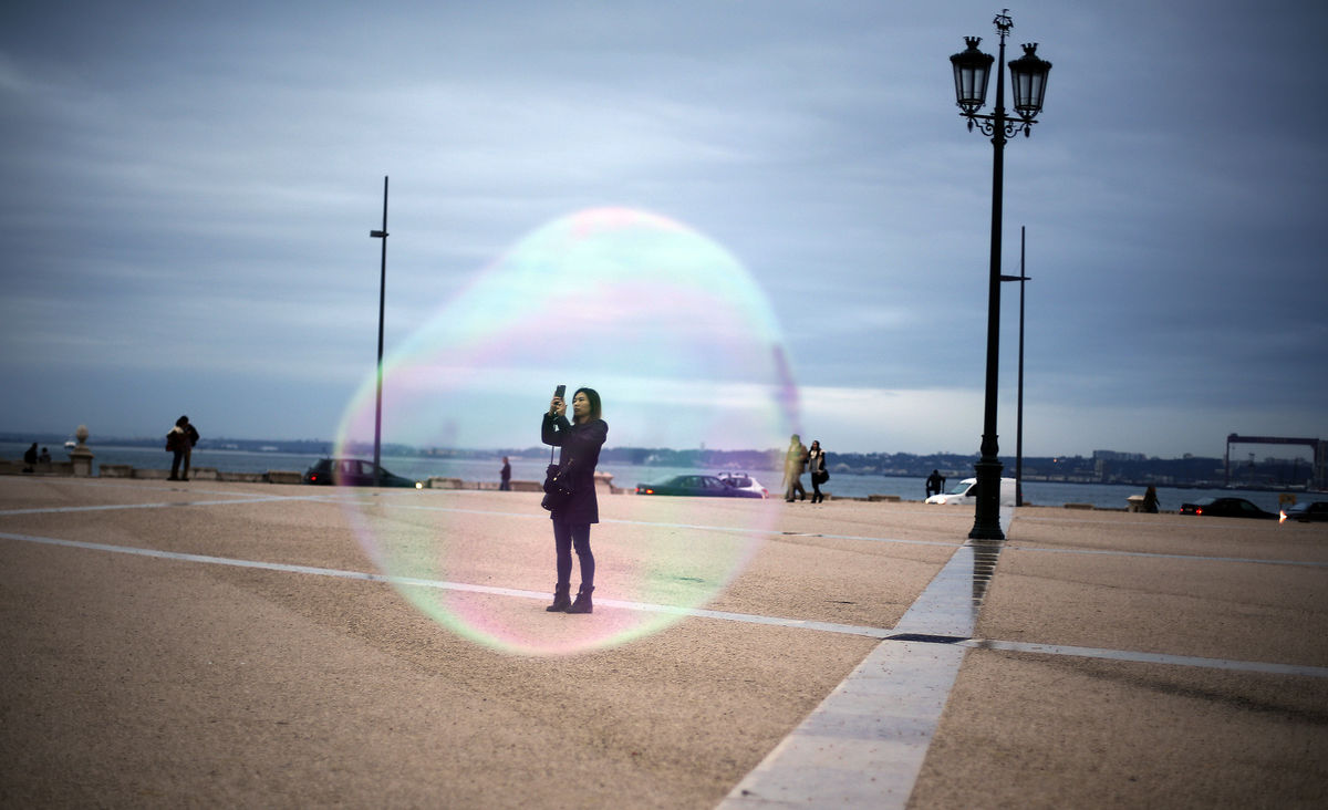 A tourist is seen through a soap bubble as she takes a picture at Comercio square in downtown Lisbon