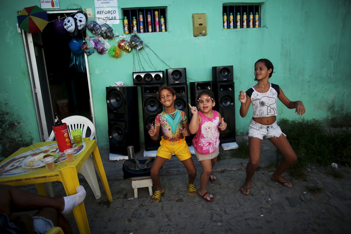 Children dance on a street near masks during one of the many carnival parties to take place in the neighbourhoods of Recife