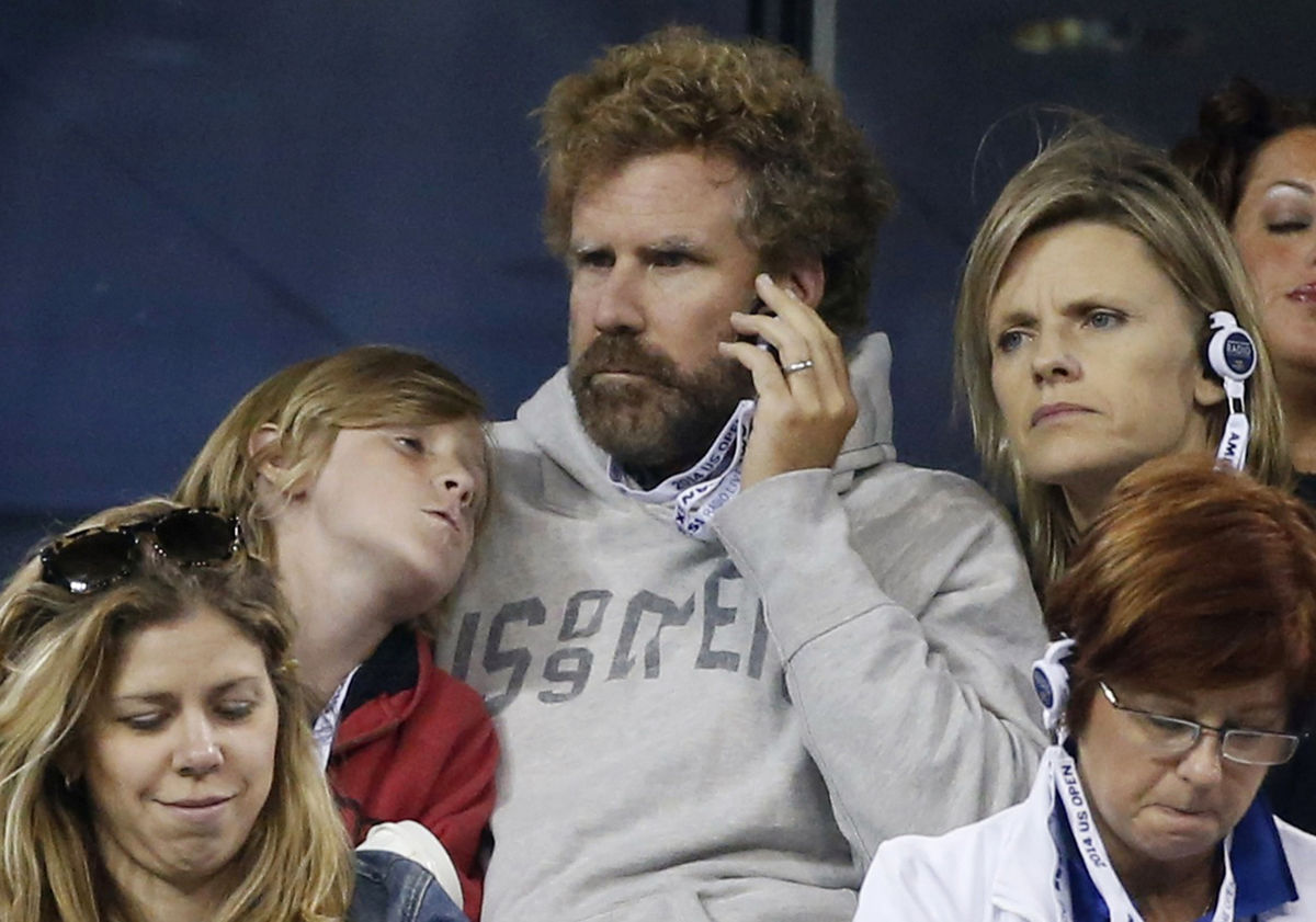 Actor Will Ferrell listens to a radio as he watches an evening match with his son and wife Viveca Paulin at the 2014 U.S. Open tennis tournament in New York