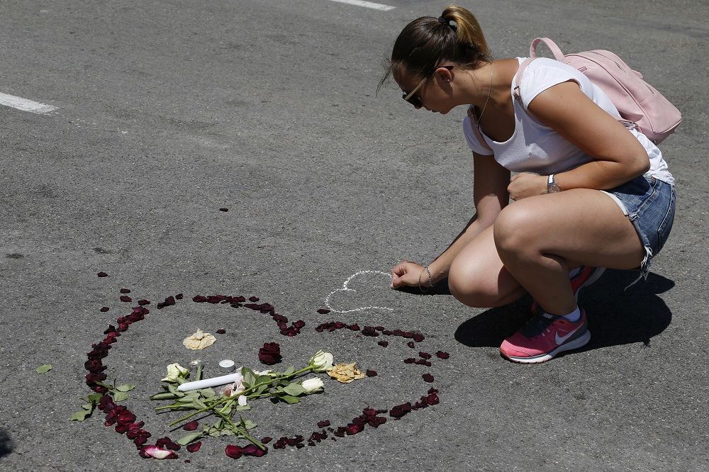 A woman draws near flower petals that form a heart placed on the road in tribute to victims of the truck attack along the Promenade des Anglais on Bastille Day that killed scores and injured as many in Nice