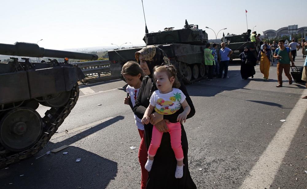 A woman with two girls walks past military vehicles in front of Sabiha Airport, in Istanbul