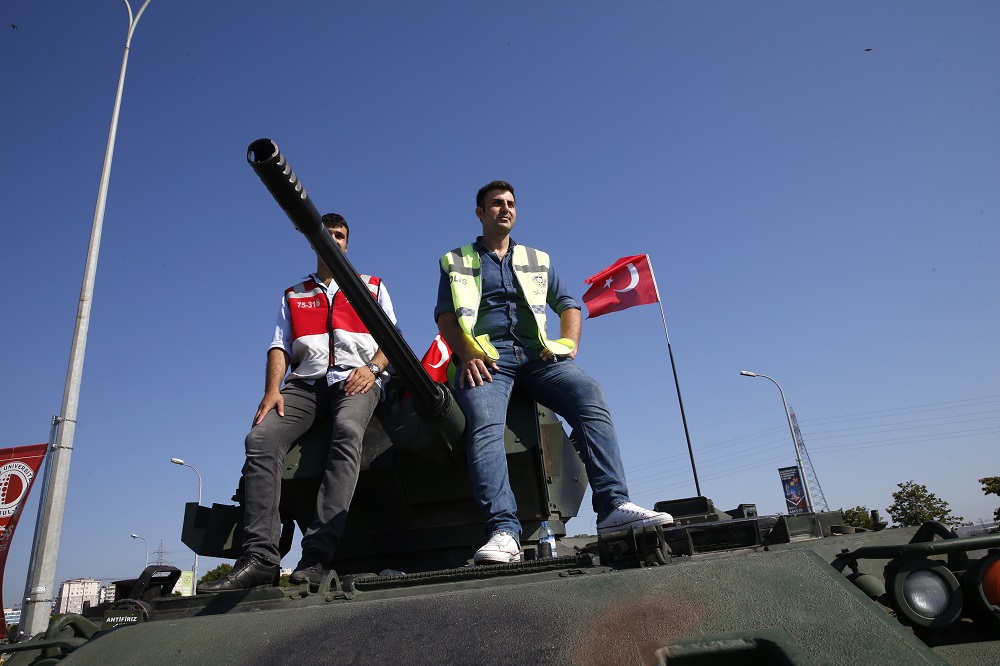 Men sit atop a military vehicle in front of Sabiha Airport, in Istanbul