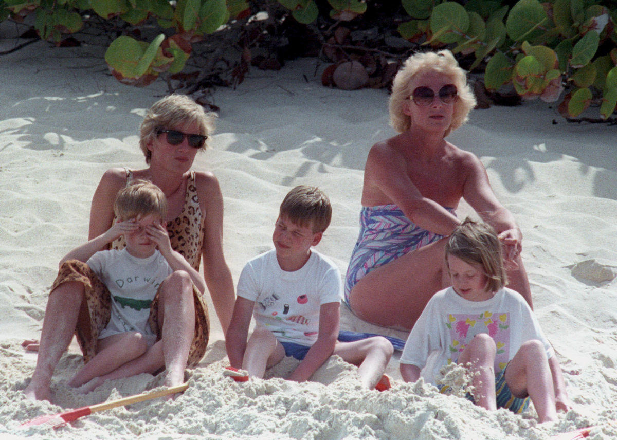 Princess Diana nurses Prince Harry on her lap as Prince William plays in the sand on a private beach on Necker Island in the British Virgin Islands