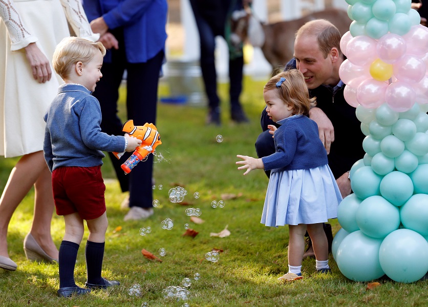 Britain’s Prince William and Princess Charlotte look on as Prince George plays with a bubble gun at a children’s party at Government House in Victoria