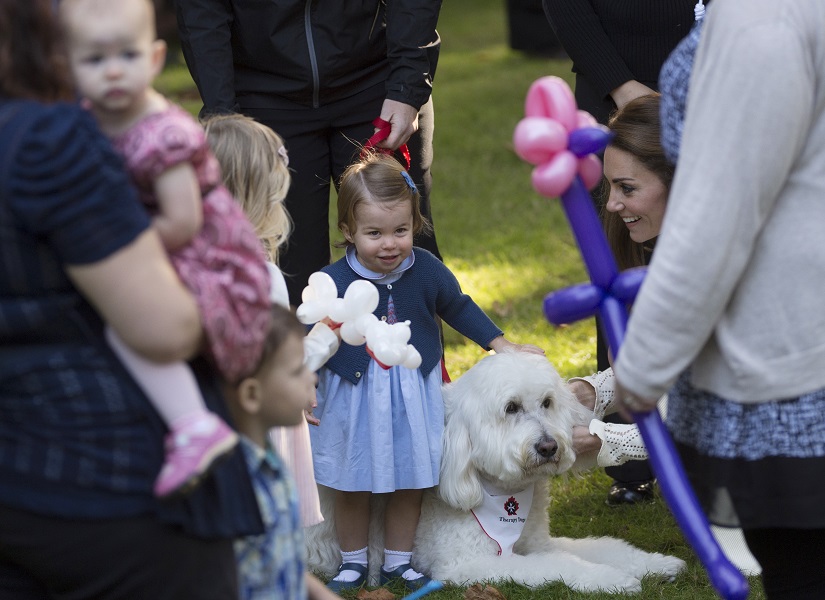 Princess Charlotte pets a dog as her mother the Duchess of Cambridge watches during a children’s party in Victoria