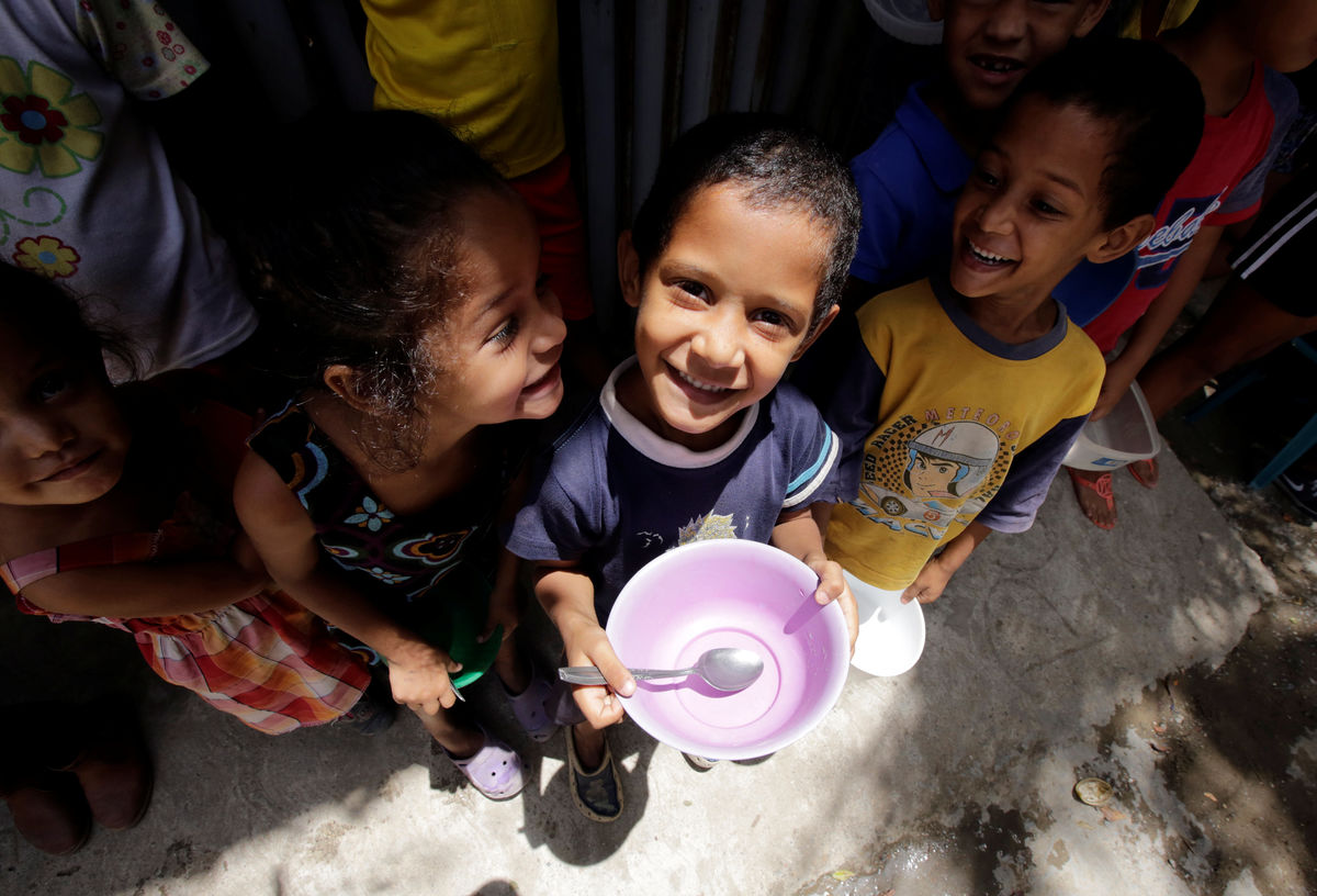 Children queue as they wait to receive free food which was prepared by residents and volunteers on a street in the low-income neighborhood of Caucaguita in Caracas