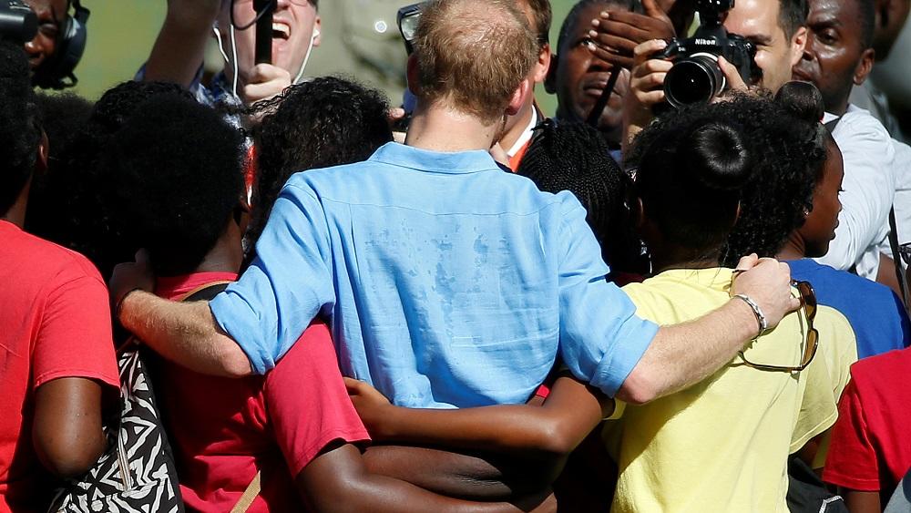 Prince Harry is hugged by a group of youths at a cricket pitch during his official visit in St. Johns