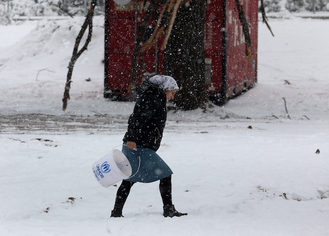 A stranded Syrian refugee braves a snowstorm at a refugee camp north of Athens
