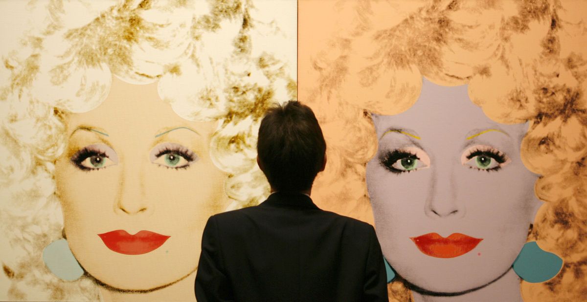 A gallery attendant stands in front of canvas prints of singer and actress Dolly Parton during the setting up of an Andy Warhol exhibtion in the National Gallery Complex in Edinburgh, Scotland