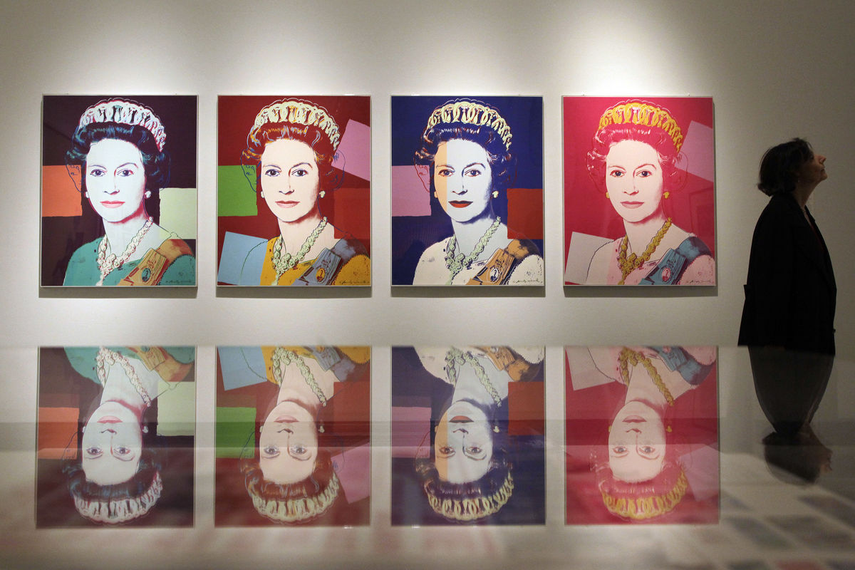 A woman stands next to silkscreen prints of Britain’s Queen Elizabeth by Andy Warhol during a press view at the National Portrait Gallery in London