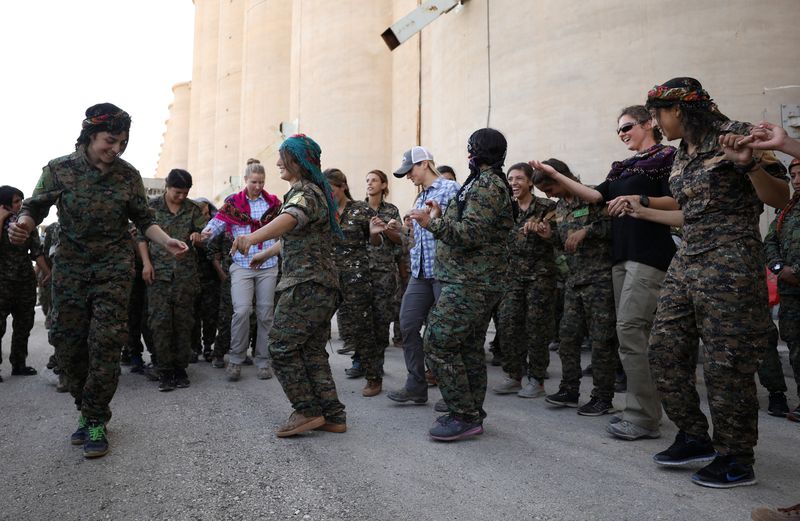 Syrian Democratic Forces female fighters dance with trainers during a graduation ceremony in the city of Hasaka