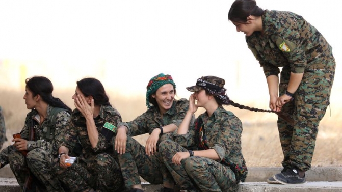Syrian Democratic Forces female fighters sit together on a curb in the city of Hasaka