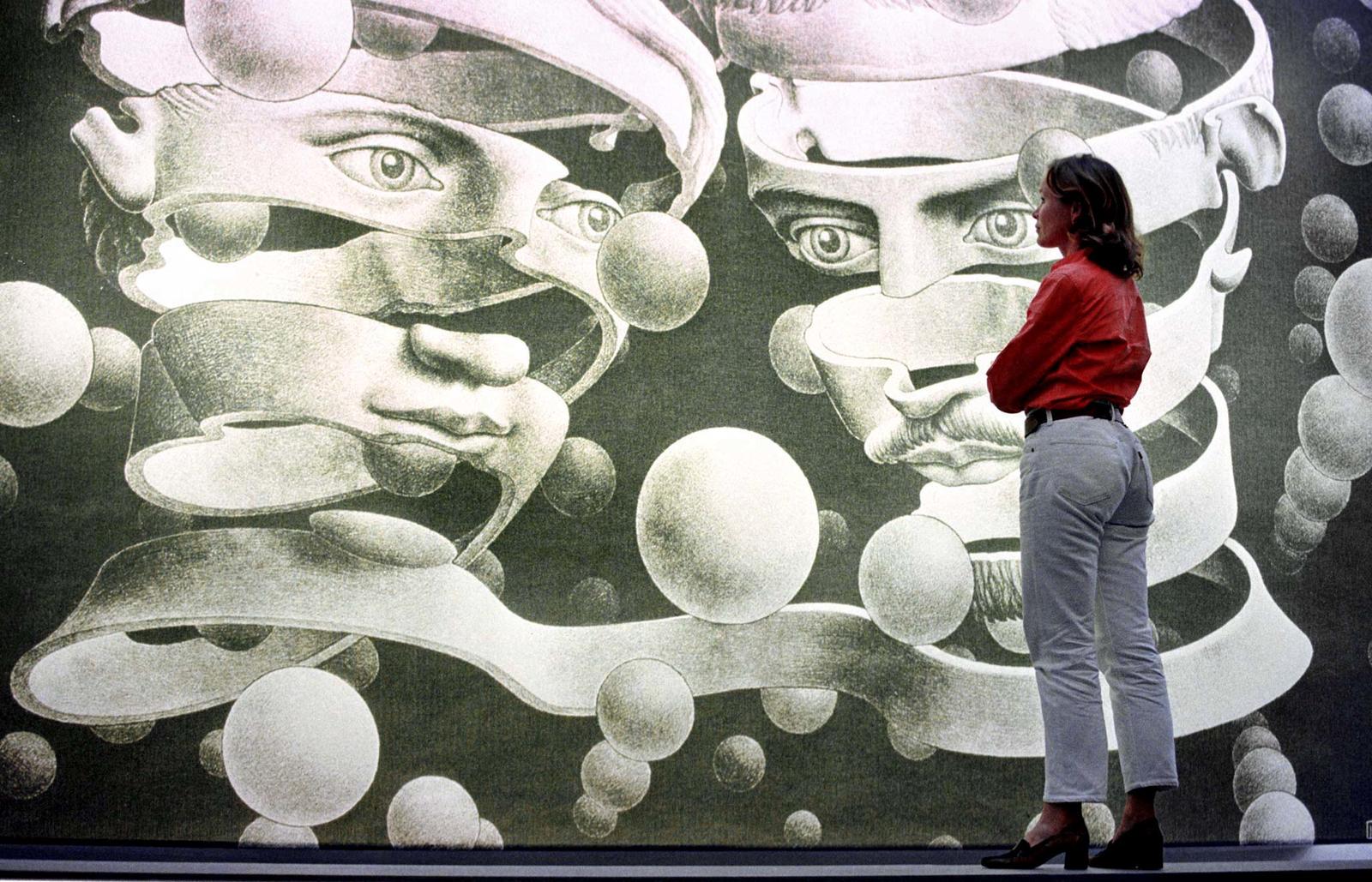 A WOMAN LOOKS AT A GIANT BACK-LIGHT BLOW UP OF M.C. ESCHER’S “BOND” AT THE ESCHER EXHIBITION IN …