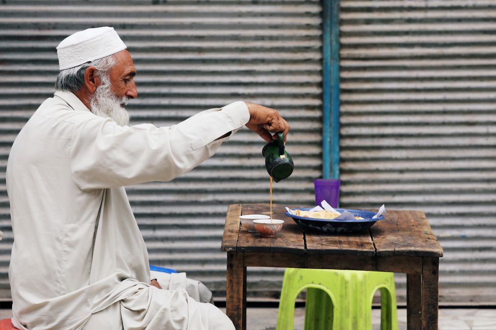 A man fills a cup of tea while having breakfast with paratha flatbread, outside closed shops in Peshawar,