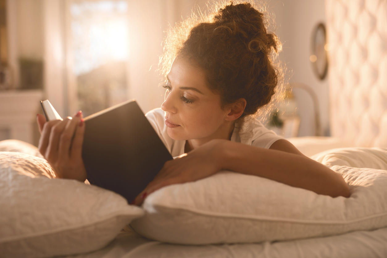 Relaxed woman reading a book in her bed.