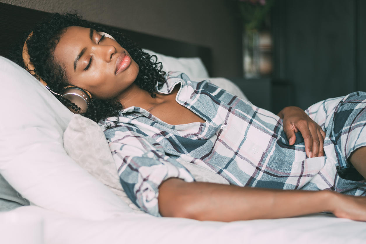 woman sleeping on bed and listening music with headphones and smartphone