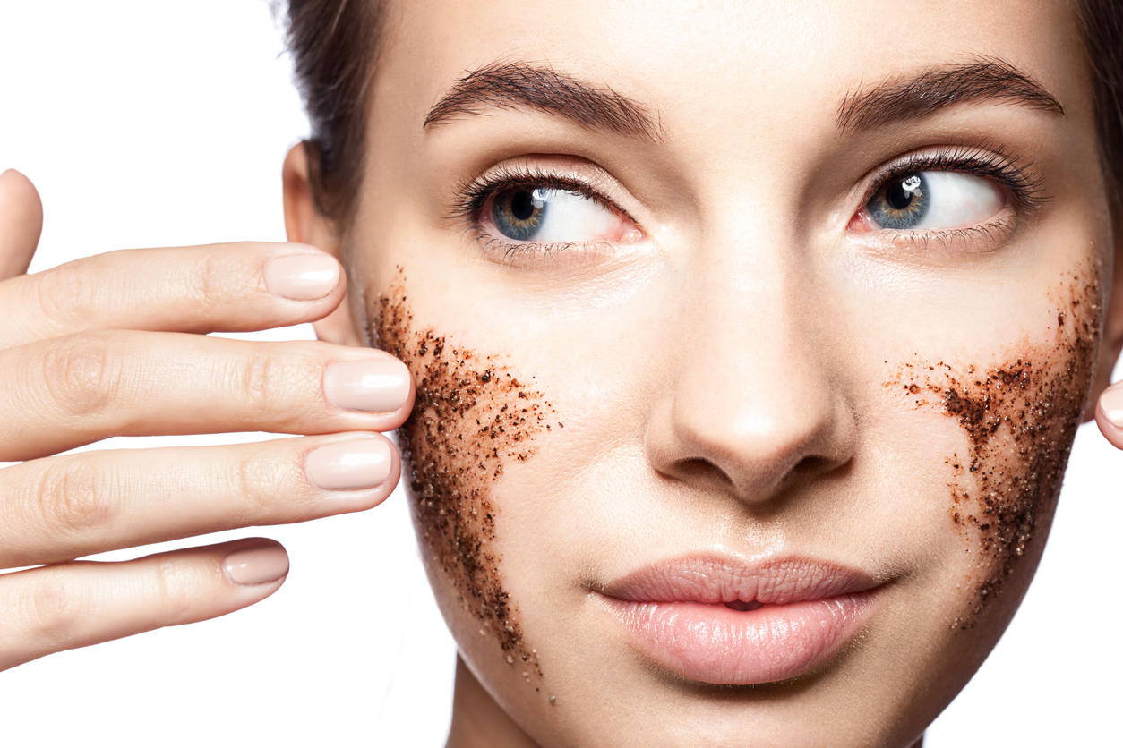 Close-up portrait of a beautiful woman with a coffee scrub on her face doing peeling skin isolated on white background