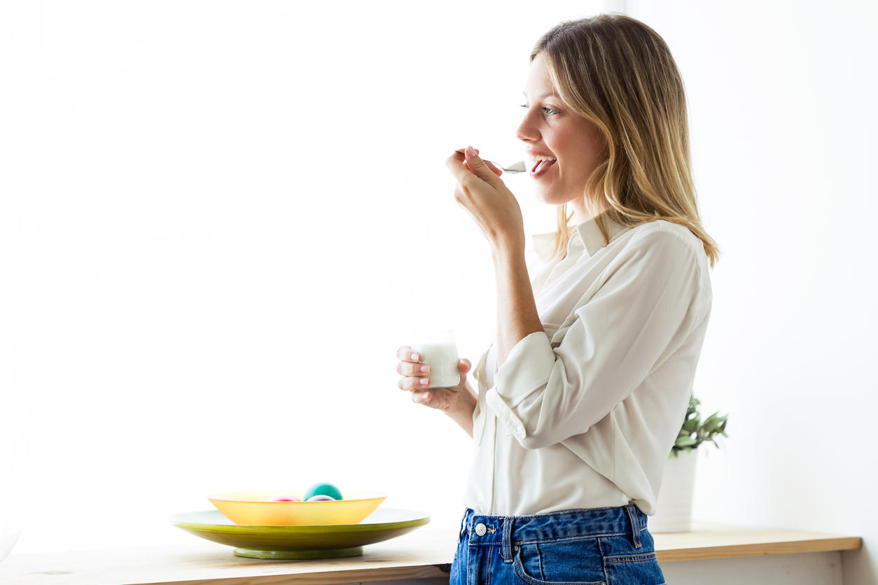 Beautiful young woman eating yogurt at home.