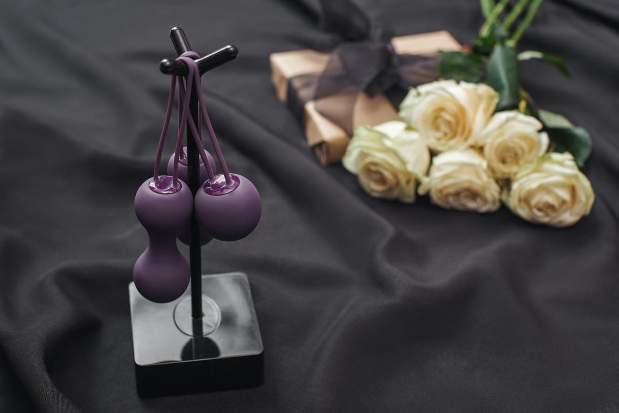 Pleasure yourself. Close up photo of purple kegel balls set for women and white roses