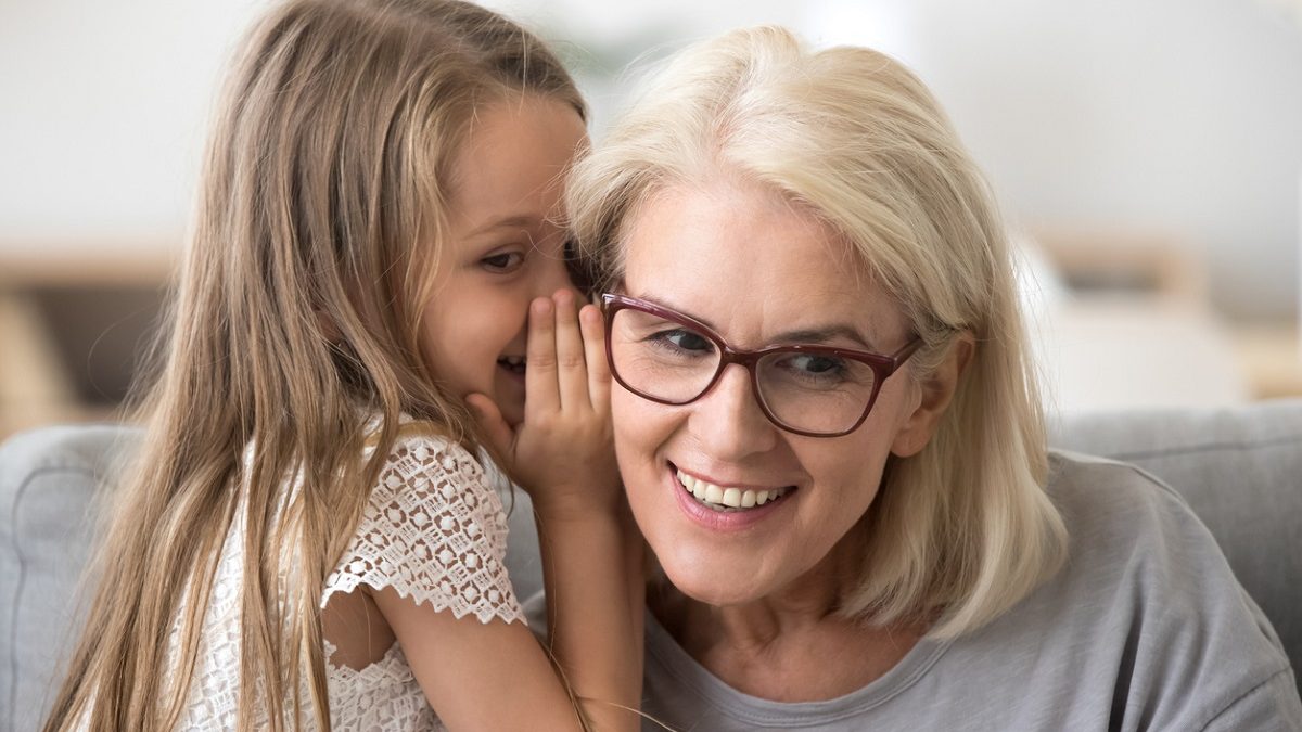 Cute little granddaughter whispering in ear telling secret to grandma