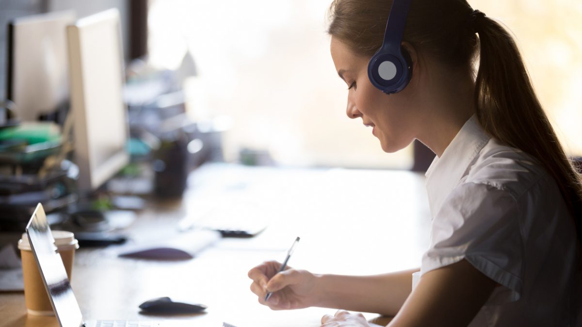 Focused woman wearing headphones write notes study online with teacher
