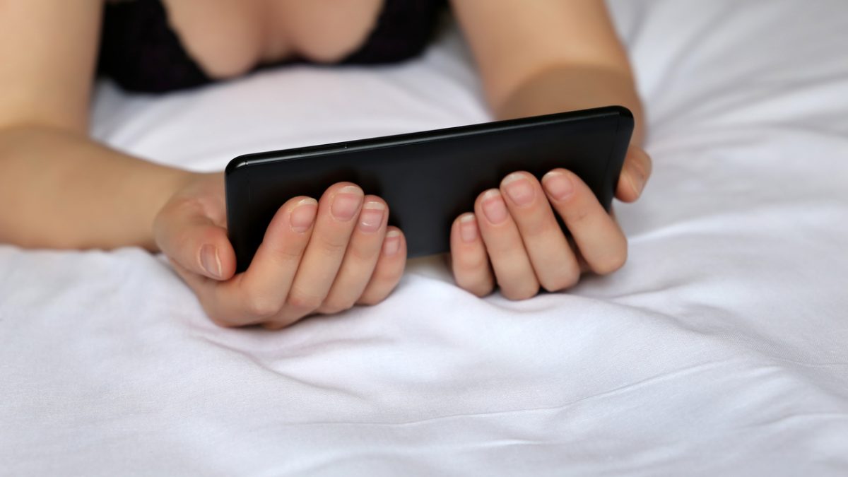 Woman in negligee lying on the bed with a smartphone in her hands