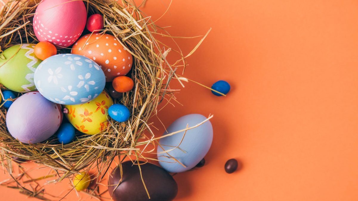 Colorful easter eggs with chocolate and candies in a nest on a orange background