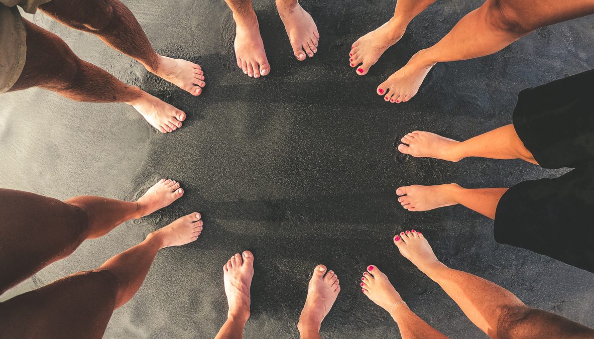 Family picture, all feet together on a beach with black sand. Top view of a group of people standing in a circle barefoot. Mother, father and sons enjoying summer holiday. Togetherness, unity concept