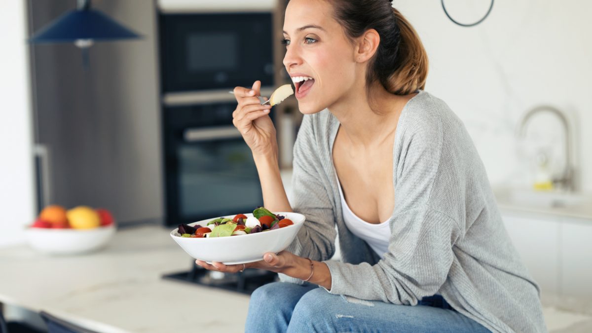 Pretty young woman eating salad while sitting in the kitchen at home.