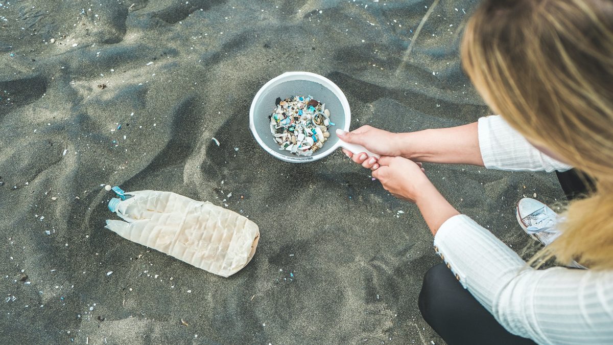 Young woman cleaning microplastics from sand on the beach - Environmental problem, pollution and ecolosystem warning concept - Focus on plastic garbage inside the net