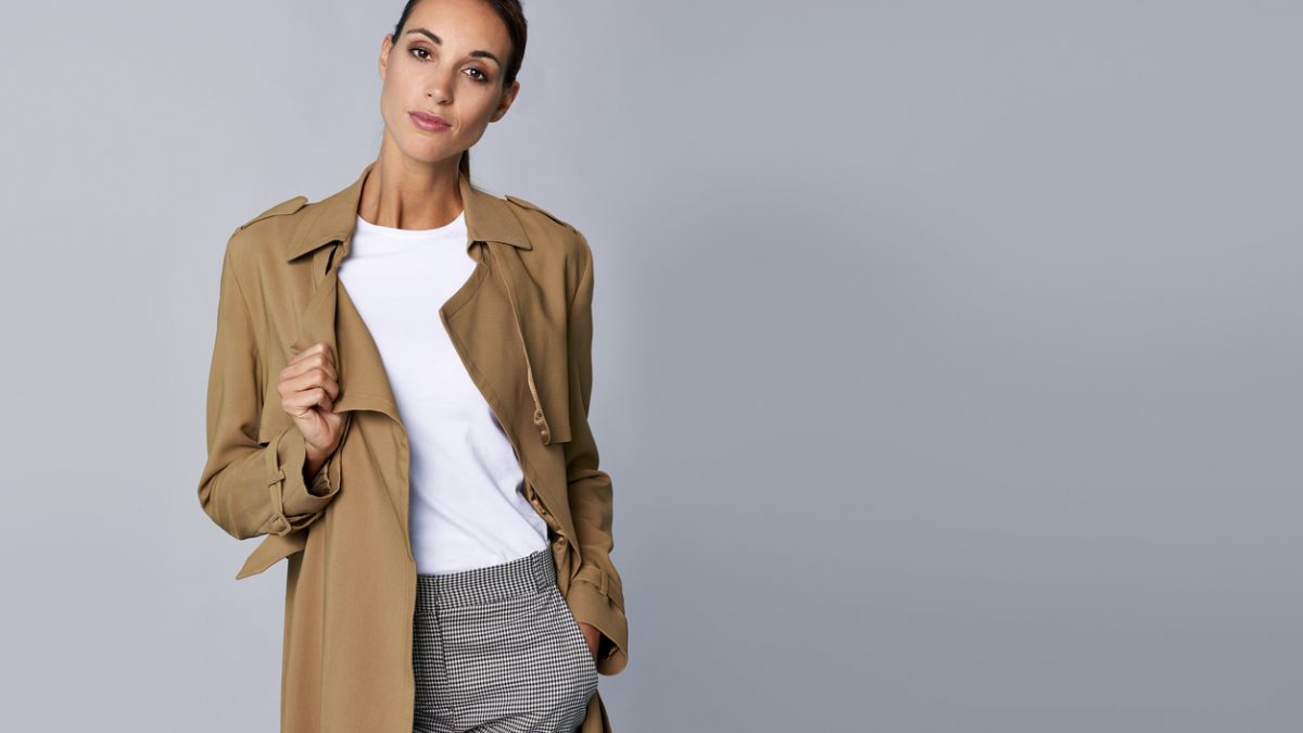 Confident young woman holding brown trench coat